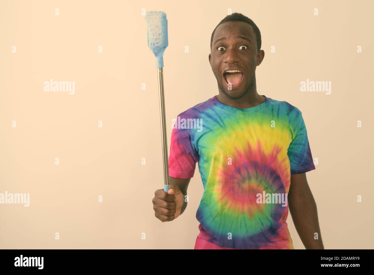Studio-Aufnahme von jungen schwarzen afrikanischen Mann suchen aufgeregt und Glücklich, während die Reinigungsbürste vor weißem Hintergrund gehalten wird Stockfoto