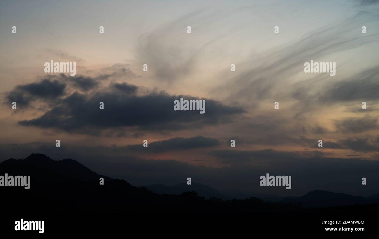 Dunkle Wolken über schwarzen Hügeln bei Dämmerung Stockfoto