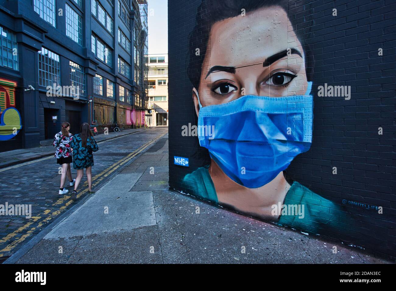 GROSSBRITANNIEN / England / London /zwei Frauen, die in London an einem Stück Straßenkunst vorbeigehen, in dem eine Krankenschwester des NHS mit einer Gesichtsmaske dargestellt ist. Stockfoto