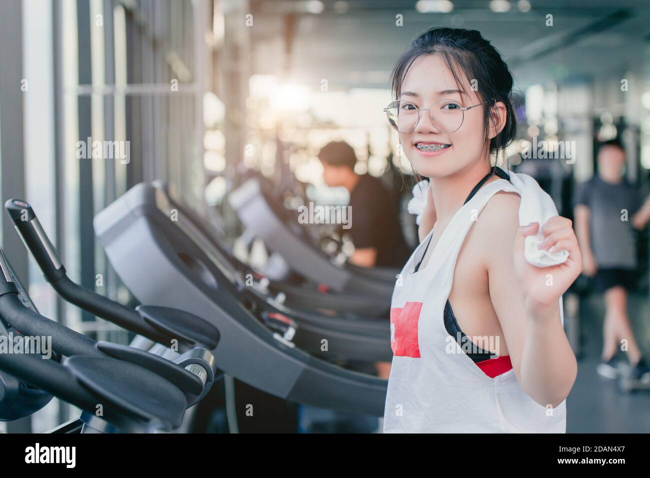 Asiatische Teenager Zahnspange Mädchen Cardio-Training Übung im Sportverein Mit einem Handtuch auf den Schultern lächelnd nach dem Training auf dem Laufband In der Turnhalle suchen Camcorder Stockfoto