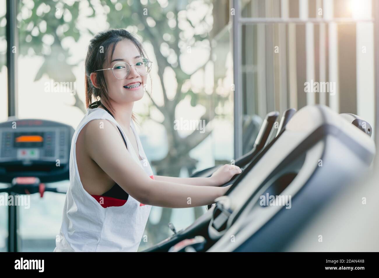 Asiatische Zahnspange Frau Kardio-Training Übung im Sportverein Trainieren Sie beim Gehen und Laufen auf dem Laufband im Fitnessstudio Blick Kamera Lächeln in der Mo Stockfoto