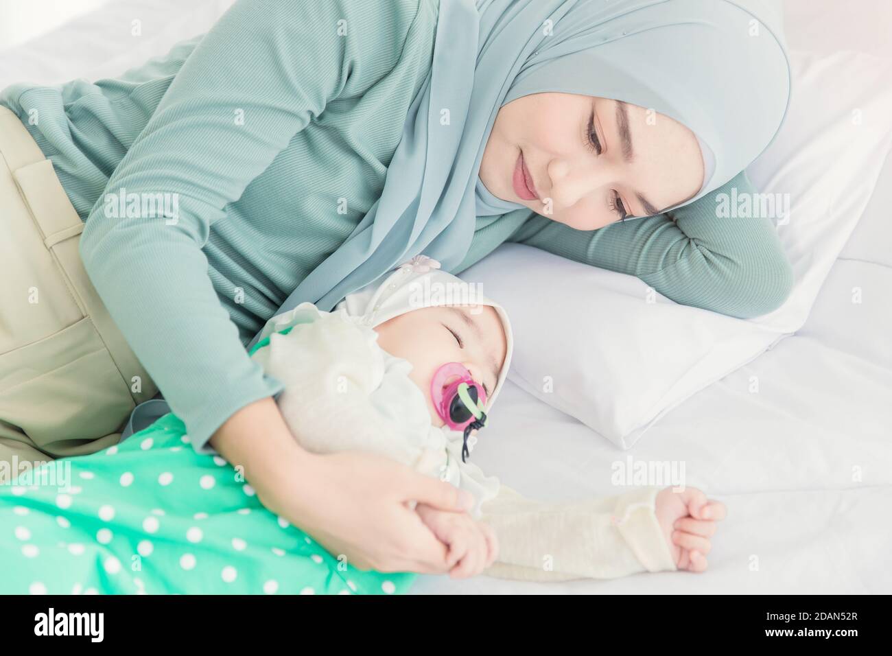Muslim Hijab Mutter suchen und kuscheln schlafen Baby mit Liebe und Sorgfalt auf dem Bett. Stockfoto