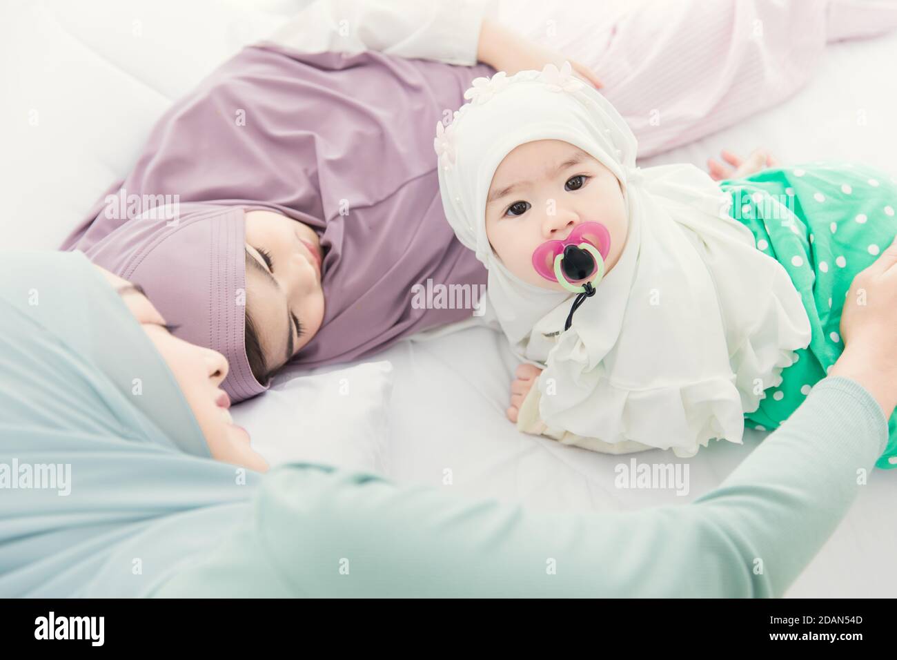 Muslimische Familie Baby mit älteren Schwester und Mutter zusammen auf dem Bett zu Hause liegen. Stockfoto