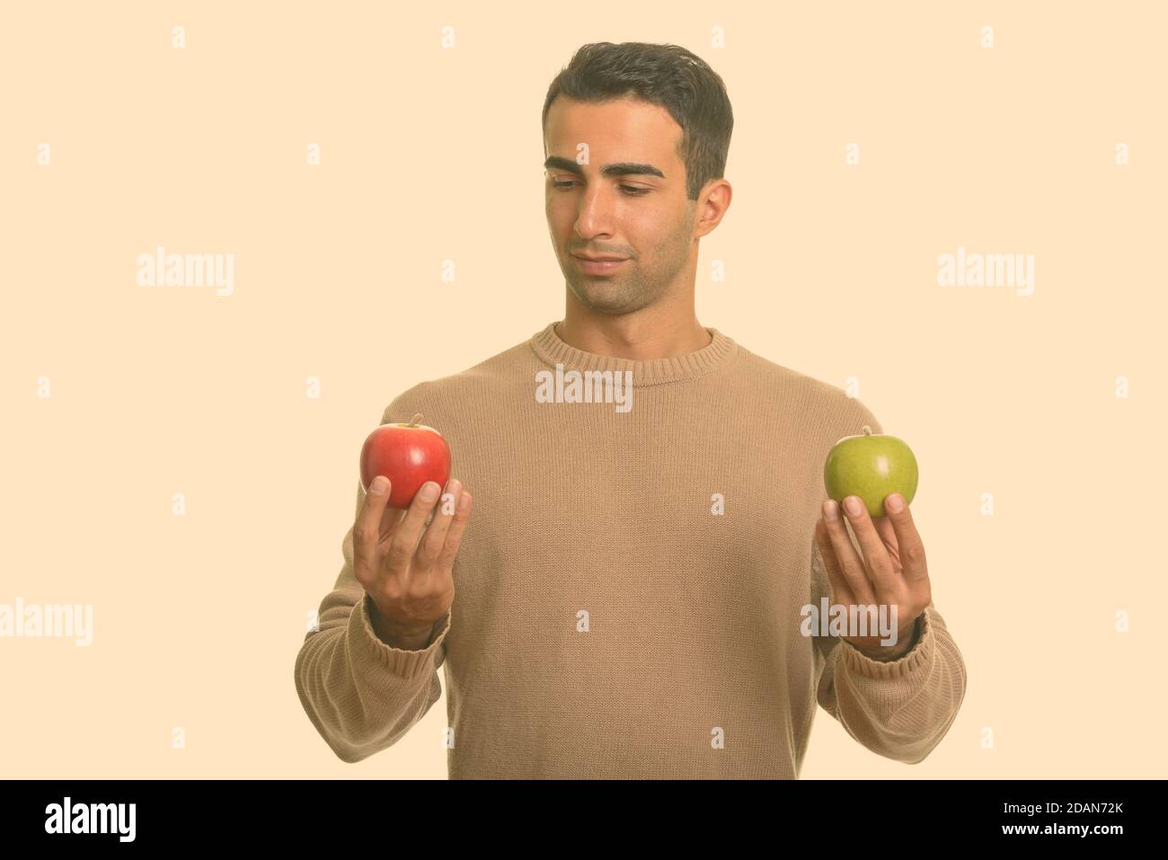 Junger hübscher Iraner, der zwischen rotem und grünem Apfel wählt Stockfoto