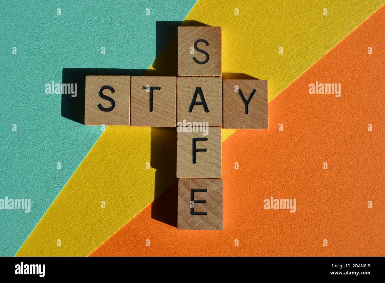 Bleiben, sicher, Wörter in Holzalphabet Buchstaben in Kreuzworträtsel Form isoliert auf bunten Hintergrund Stockfoto