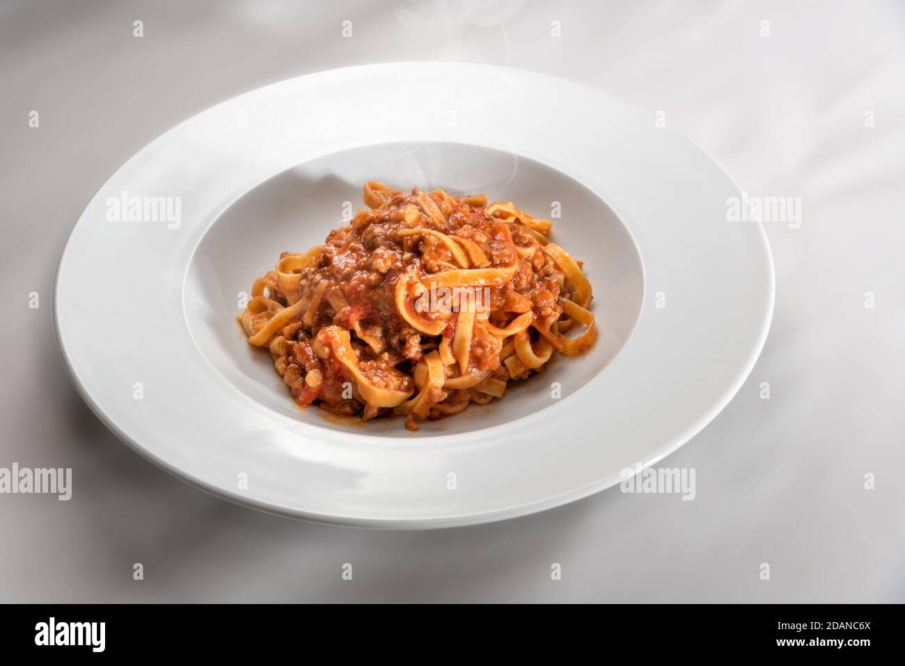 Spaghetti auf Ei-Basis (italienische Tagliatelle) mit Fleisch und Tomatensauce gekrönt, in einem Teller auf weißem Hintergrund gedämpft Stockfoto
