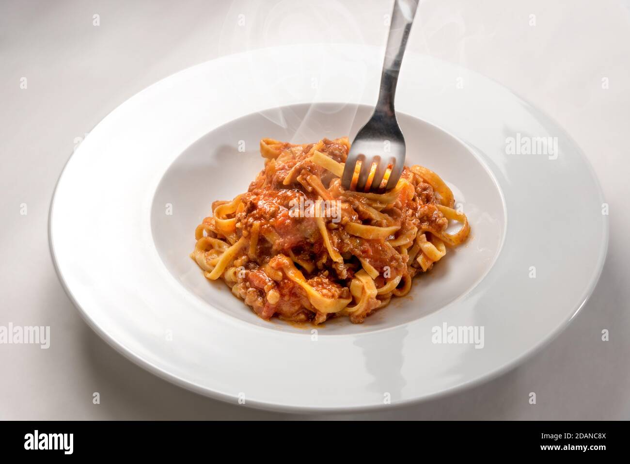 Spaghetti auf Ei-Basis (italienische Tagliatelle) mit Fleisch und Tomatensauce Whit Gabel gekrönt, gedämpft in einem Teller auf weißem Hintergrund Stockfoto