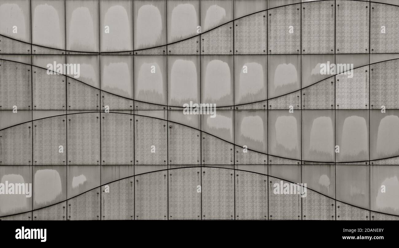 Ein Schwarz-Weiß-Bild einer modernen getäfelten und genieteten Fliesenwand mit geschwungenen Linien, die einen Welleneffekt erzeugen. Stockfoto