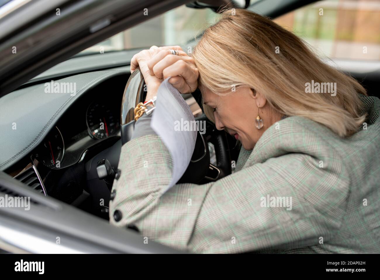 Verzweifelte reife blonde Geschäftsfrau mit Papier setzen ihren Kopf auf Steuern Stockfoto