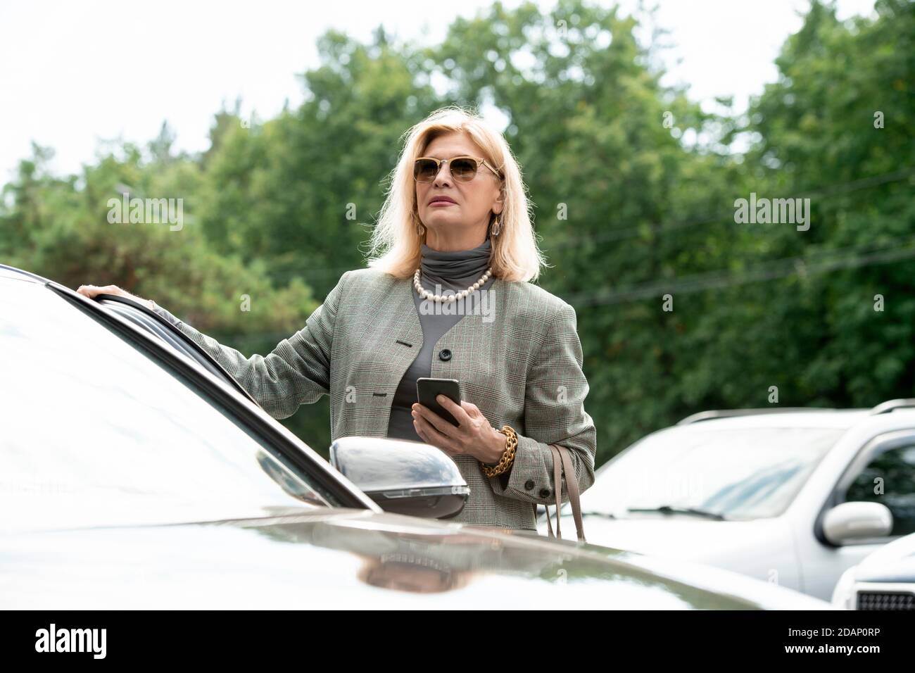 Elegante reife weibliche Geschäftsagentin mit Smartphone im Stehen Auto Stockfoto