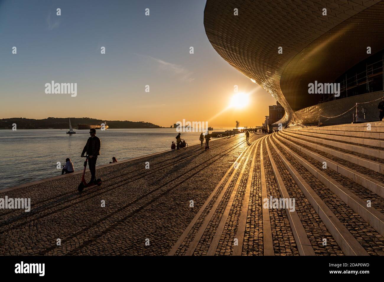 Die Silhouetten von Menschen und Schiffen bewegen sich auf dem Tejo und auf dem PAVE Walk neben Maat, Museum für Kunst, Architektur und Technologie in Lissabon, Portugal Stockfoto