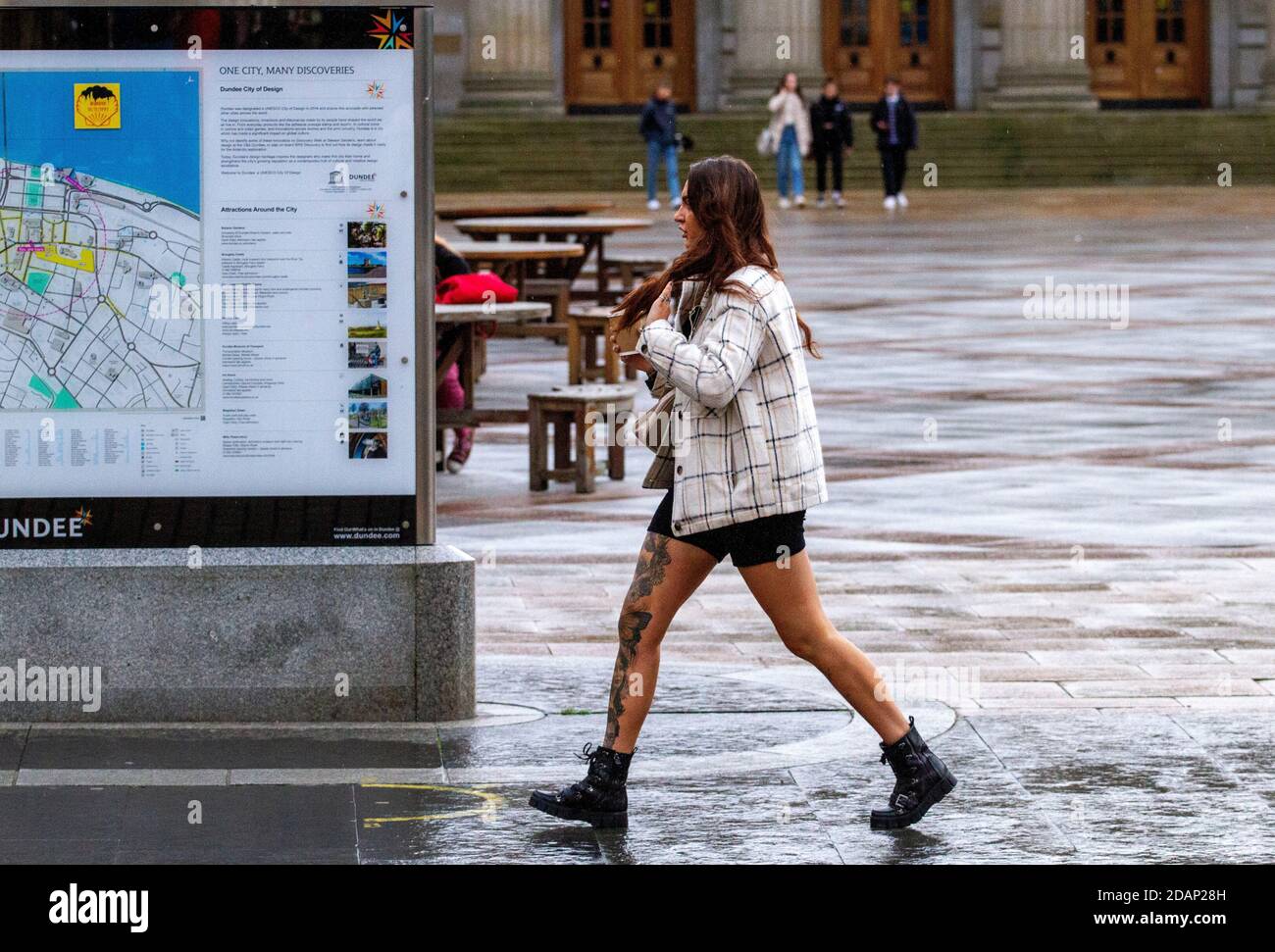 Dundee, Tayside, Schottland, Großbritannien. November 2020. UK News Covid-19 Lockdown. Menschen, die in Dundee auf den Straßen herumlaufen und nur wenige wichtige Bekleidungsgeschäfte geöffnet haben, da die strengere Stufe 3 Covid-19 Lockdown-Beschränkung durchgesetzt wurde. Eine große modische Frau mit markanten Tätowierungen auf ihrem rechten Bein ist sich der sozialen Distanzierungsrichtlinien bewusst, die im Stadtzentrum mit einer kleinen Tasse Kaffee an einem kalten und nassen November-Nachmittag gehen. Kredit: Dundee Photographics/Alamy Live Nachrichten Stockfoto