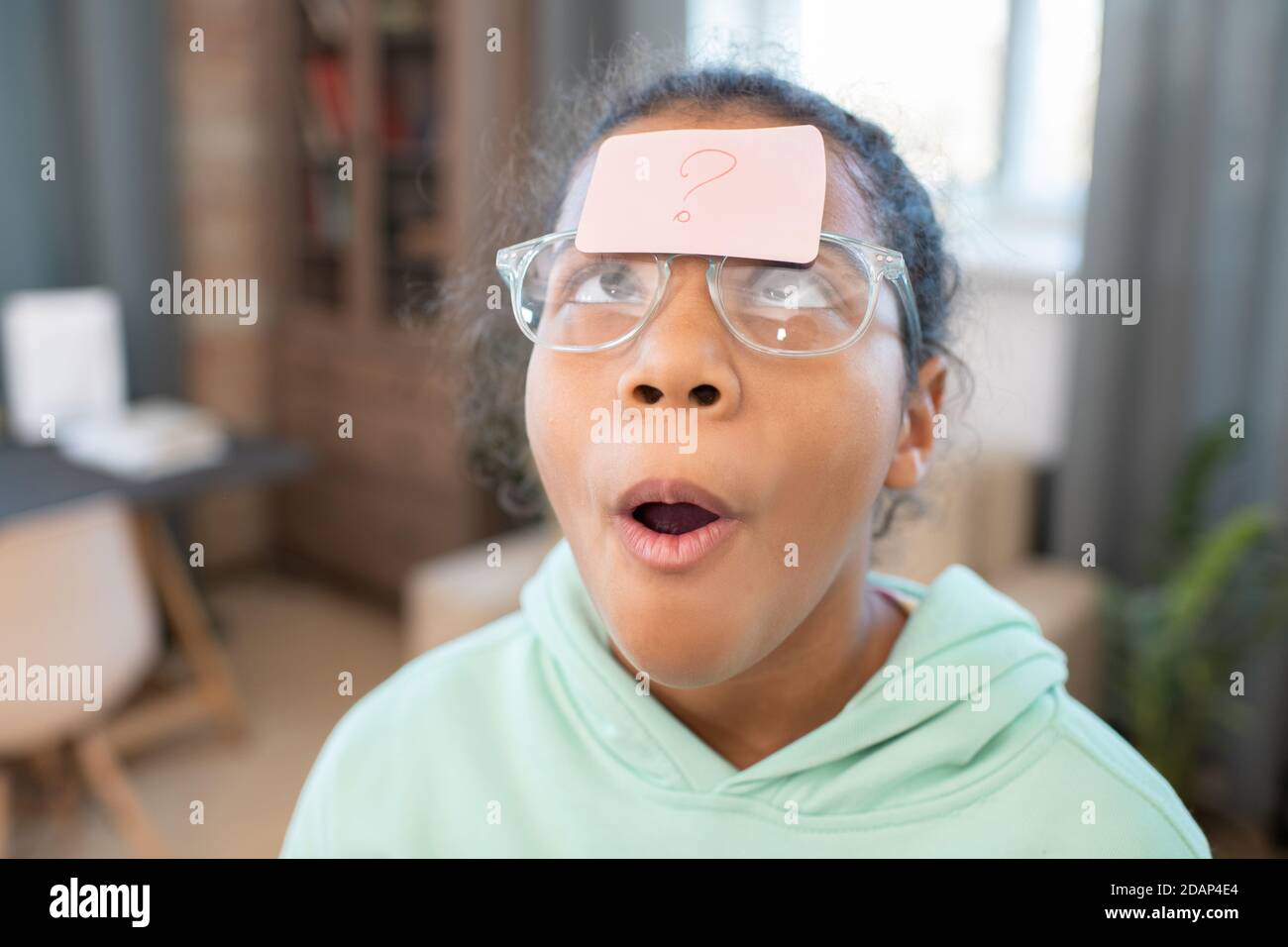 Mädchen in Brillen, die auf Notizbuch mit Fragezeichen schauen Ihre Stirn Stockfoto