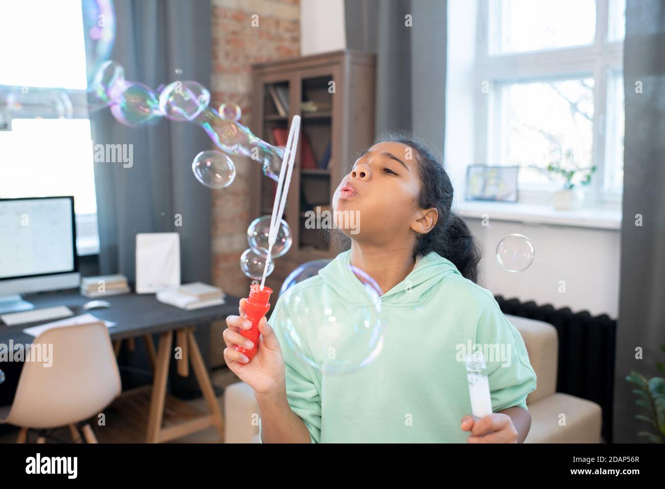 Cute Mixed-Rennen Mädchen in Casualwear Blasen Gruppe von Seifenblasen Im Wohnzimmer Stockfoto
