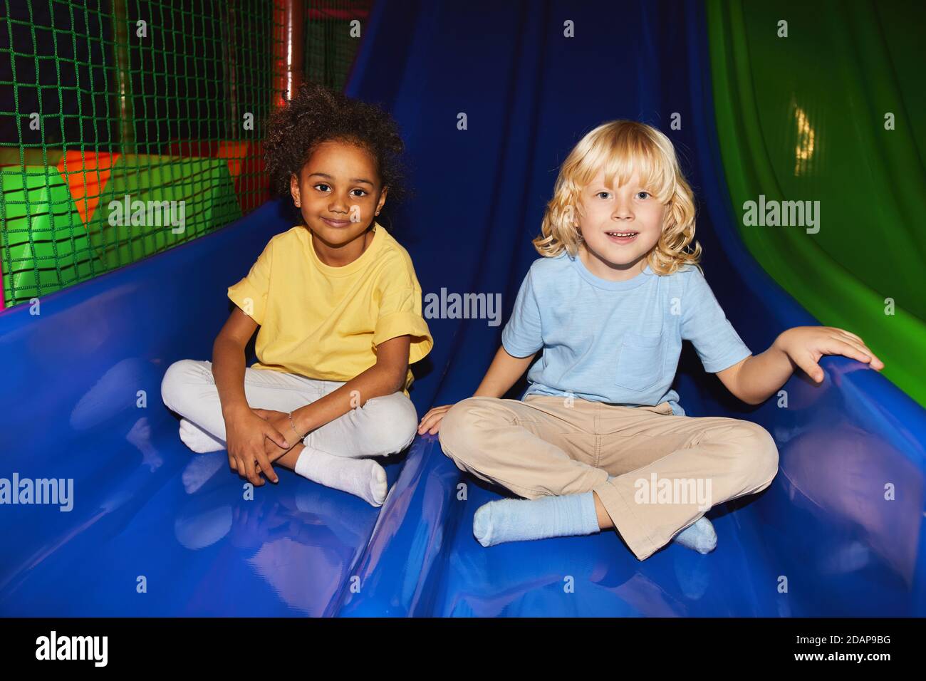 Portrait von glücklichen Kindern, die während der Fahrt auf die Kamera schauen Eine Rutsche im Spielzentrum Stockfoto