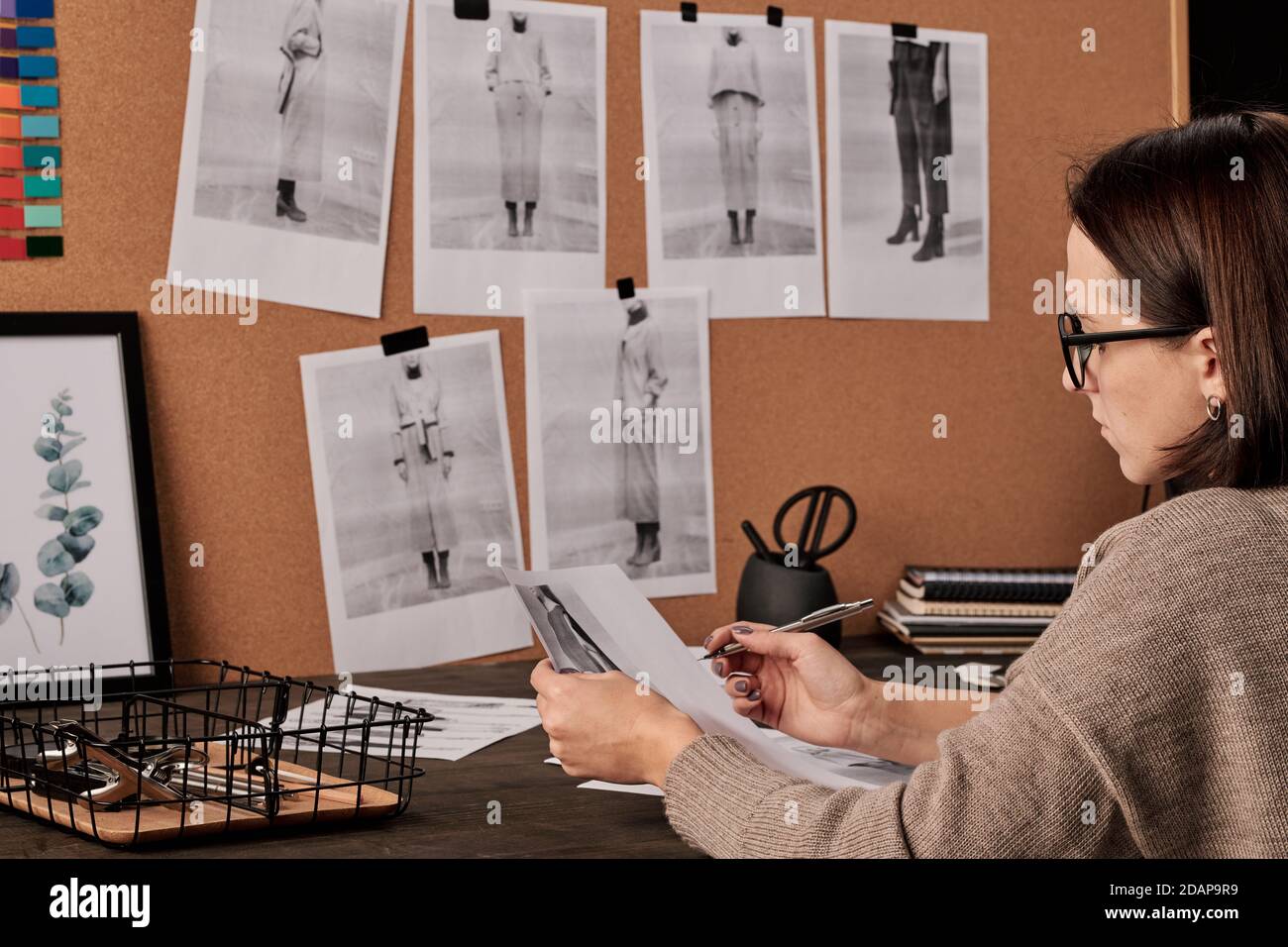 Junge zeitgenössische Modedesignerin arbeitet mit Fotos von Tisch in studio Stockfoto
