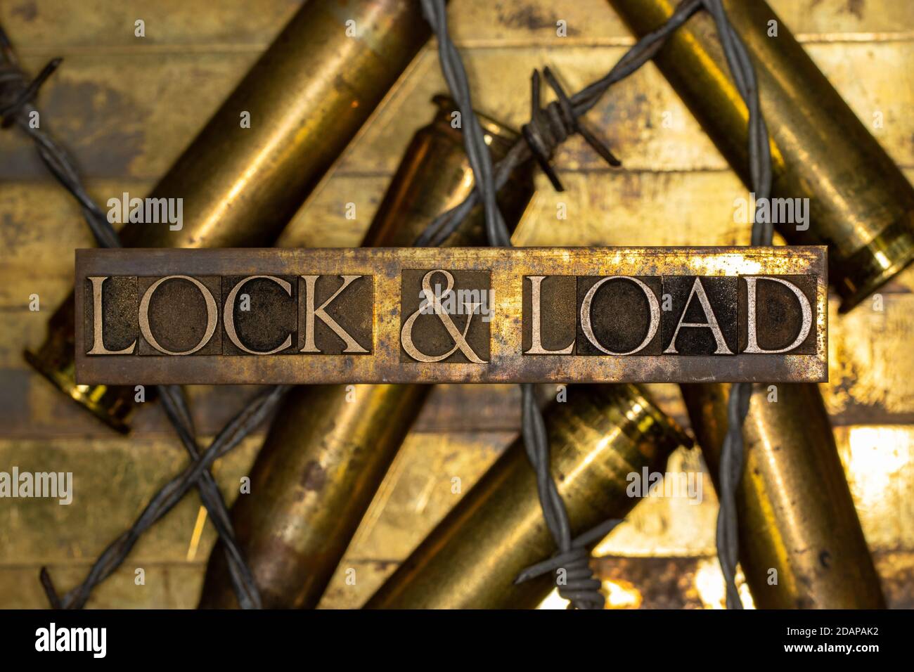 Lock & Load Text auf vintage texturierten Grunge Kupfer und Goldfarbener Hintergrund mit 50 cal Geschoss-Gehäuse mit Stachelschal ausgekleidet Draht Stockfoto