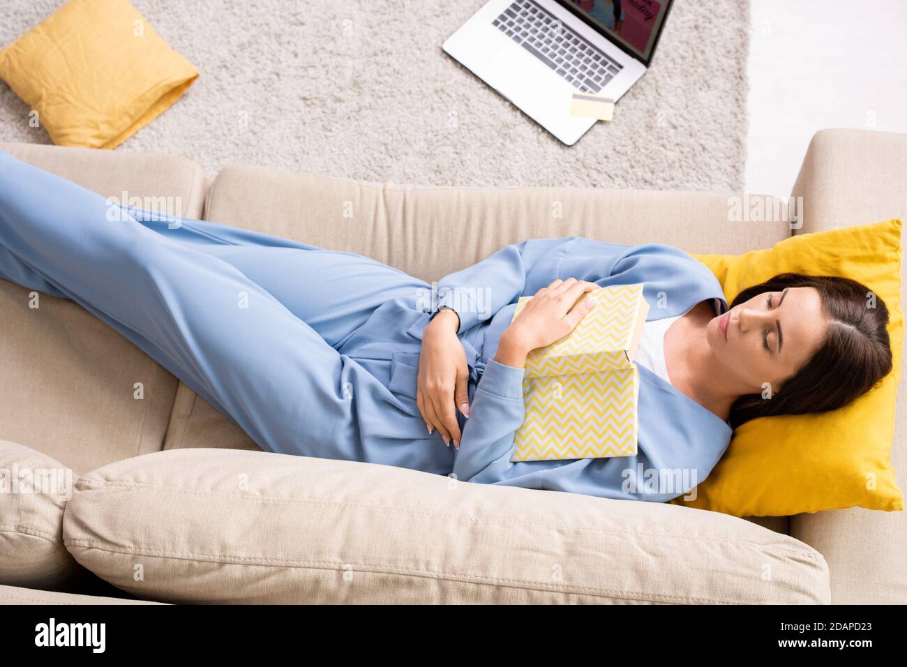 Draufsicht auf junge erholsame Frau in blauen Schlafanzug halten Buch auf der Brust öffnen Stockfoto