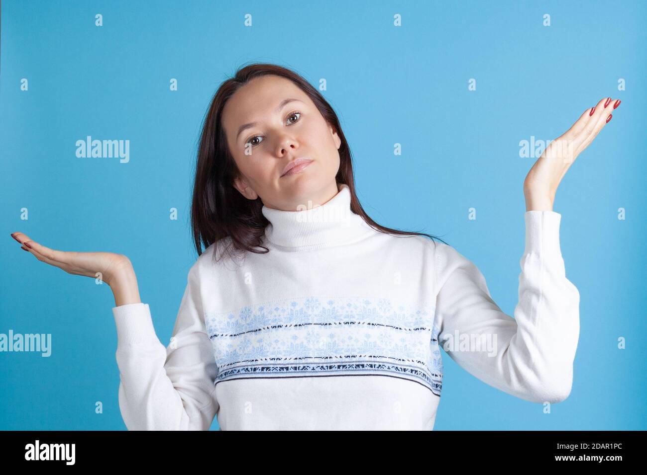Enttäuscht spreizt die zweifelende asiatische junge Frau im Pullover ihre Hände isoliert auf blauem Hintergrund Stockfoto