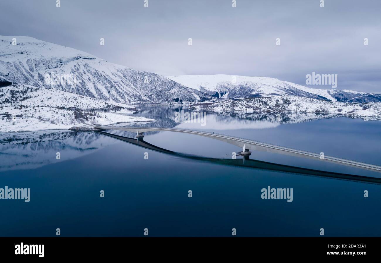 Lange Autobrücke über einen spiegelglatten blauen Fjord in einer Winterlandschaft, Gildeskal, Nordland, Norwegen Stockfoto