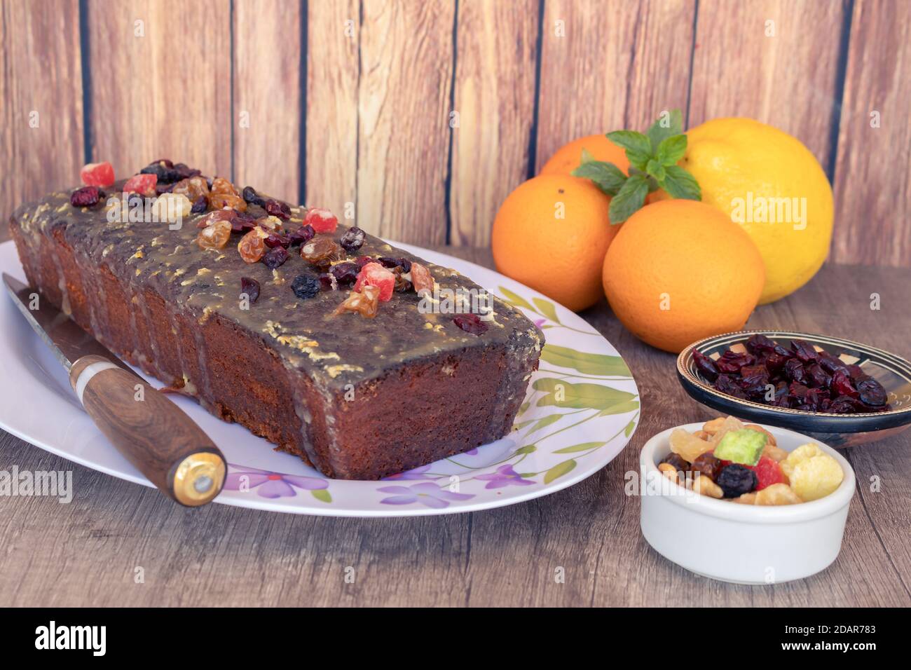 Hausgemachter Zitronen- und Orangenpudding mit Früchten auf einer weißen Platte mit Vintage-Stil Blumenzeichnungen auf einem Holztisch, einige Zitrusfrüchte und ein rustikales Stockfoto