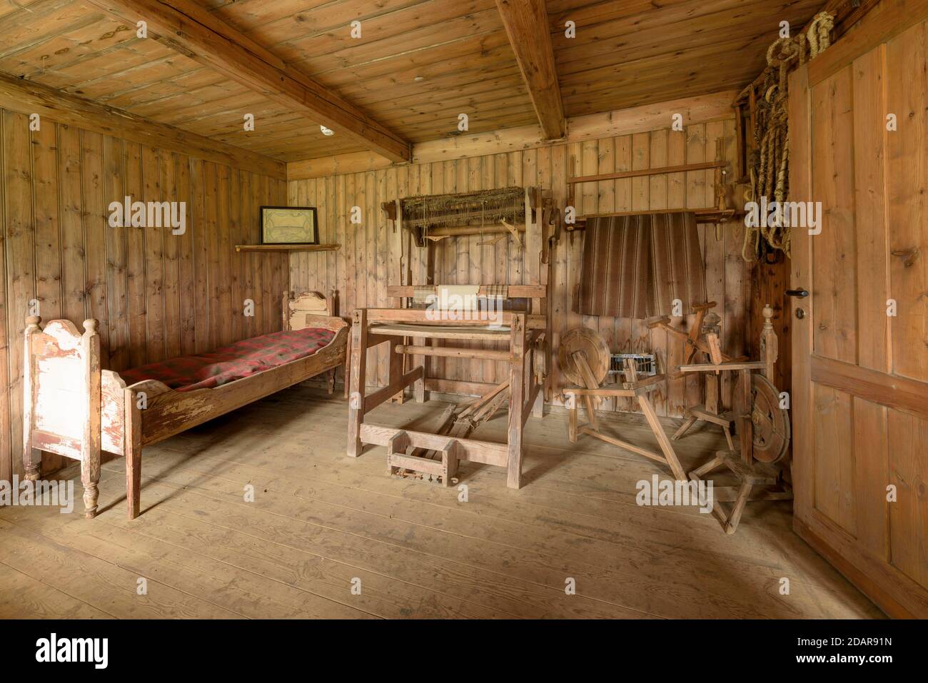 Innenansicht eines historischen Schlafzimmer mit Bett und karierter Decke, Webstuhl und Spinnrad auf einem Torfhof, Sod Haus Siedlung Grenjadarstadur Stockfoto