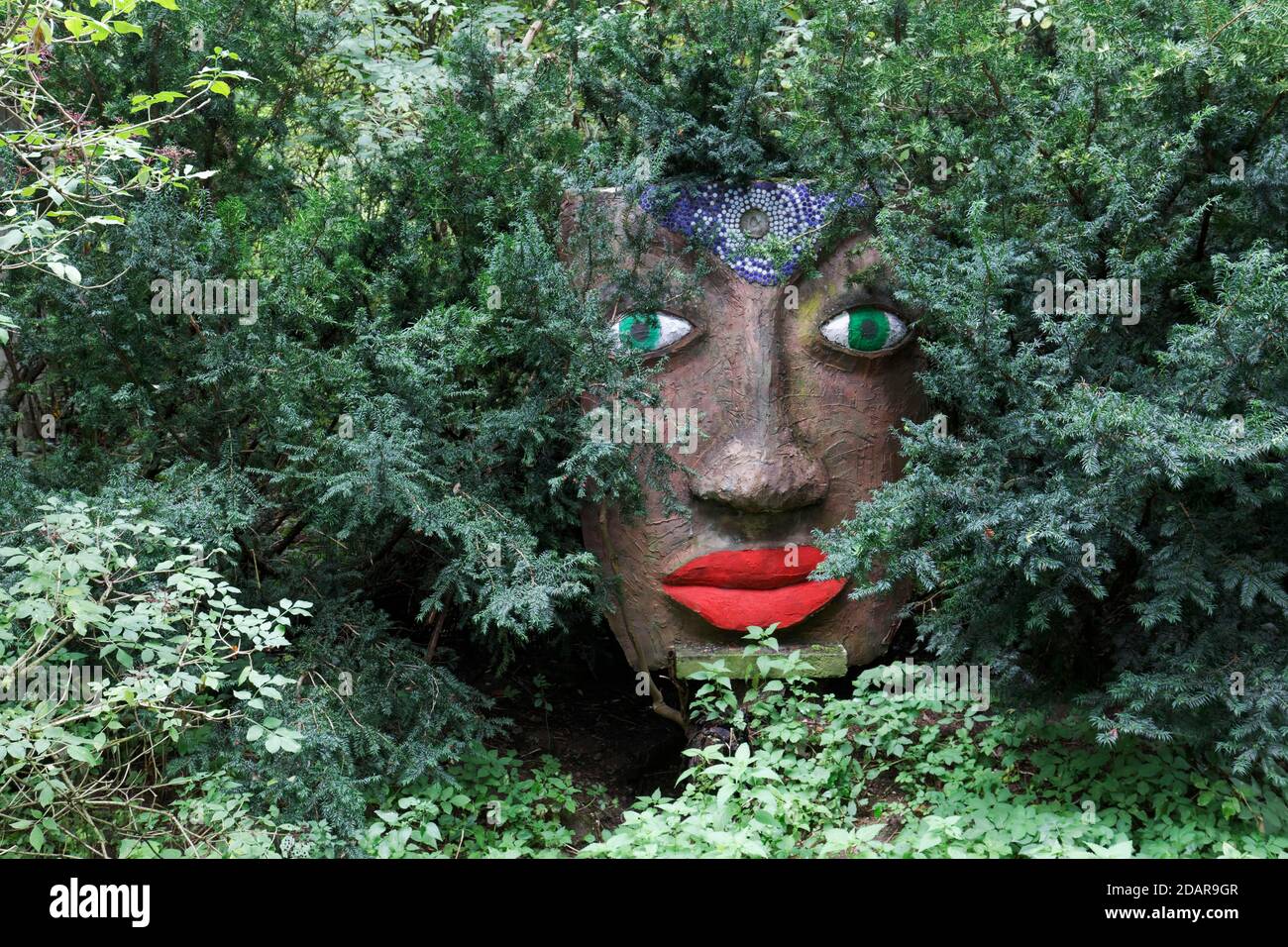 Magisches Frauengesicht mit roten Lippen und grünen Augen schaut durch Äste, Skulptur, Skulpturengarten des Künstlers Jochen Bach, Plinzmühle, Plinz Stockfoto