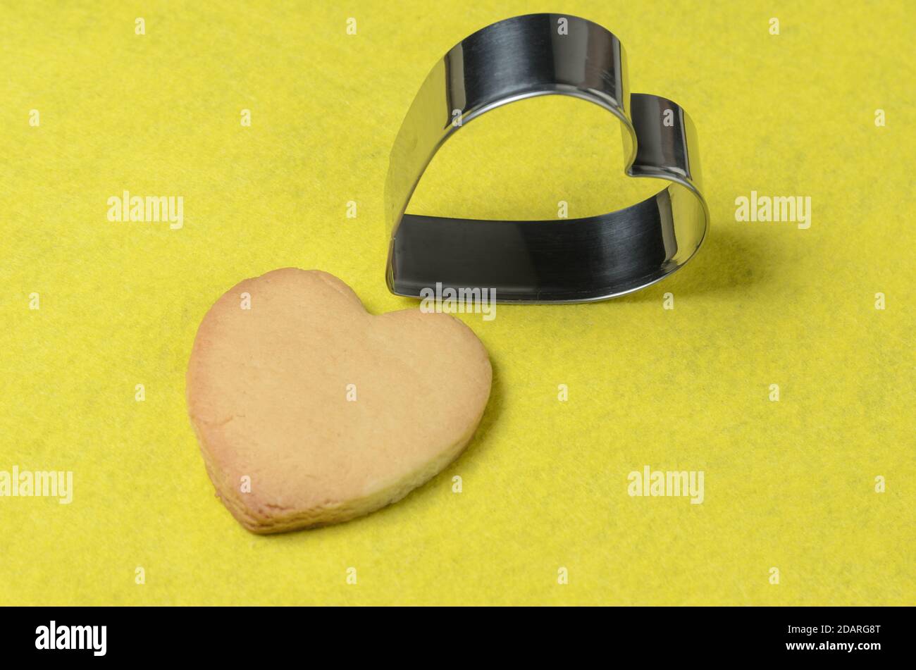 Hausgemachte Kekse mit einem Metall-Backform in Form eines Herzens auf einem gelben Hintergrund. Selektiver Fokus. Stockfoto