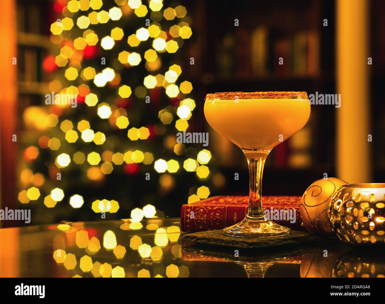 Nahaufnahme von Chocolate Orange Martini - festlicher Weihnachtscocktail mit Weihnachtsdekoration, einem roten Buch und einer Kerze auf dem Tisch, Weihnachtsbaumbok Stockfoto