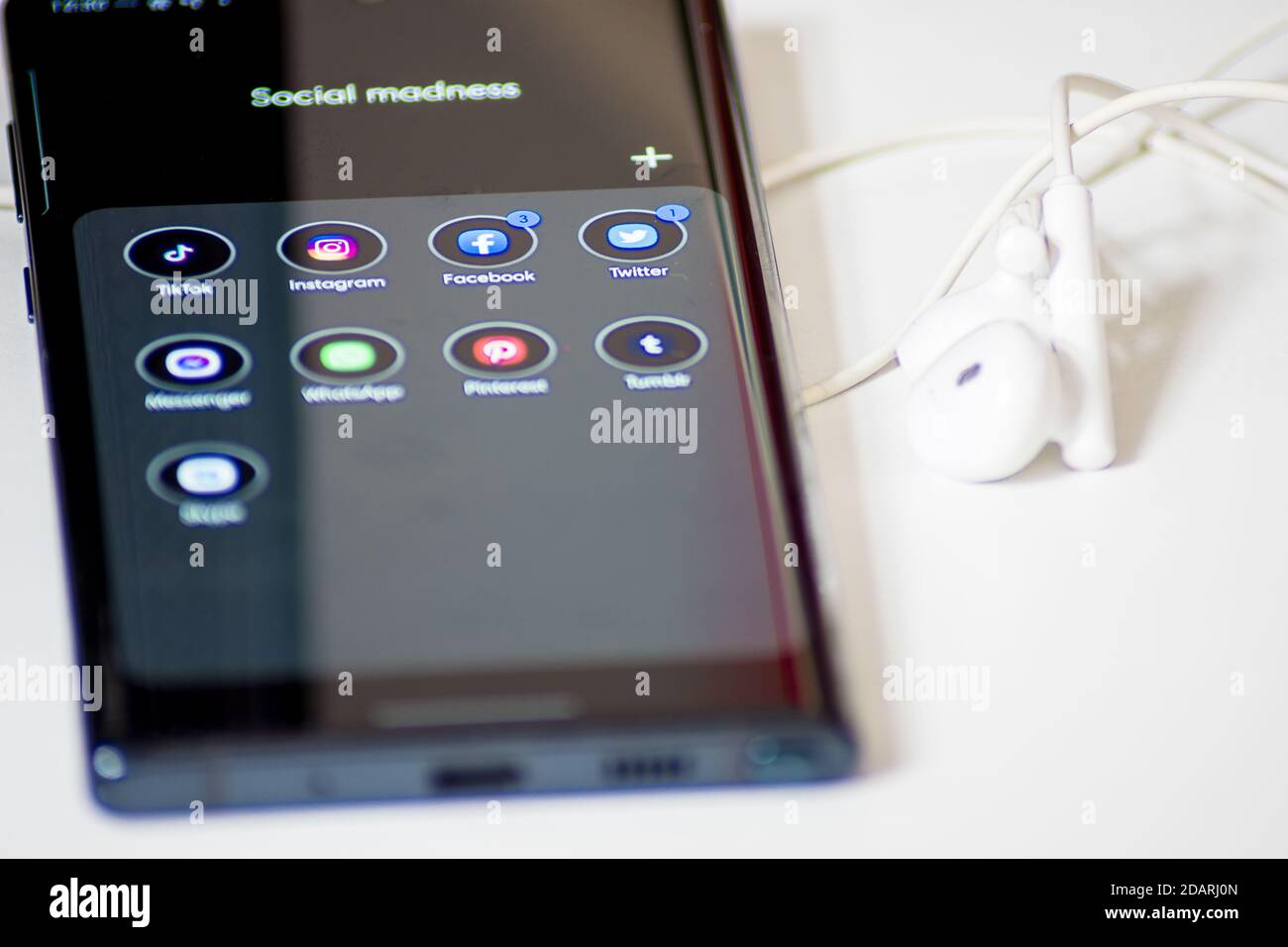 Wien / Österreich / 13. November 2020: Schwarz glänzendes Smartphone und weiße Kopfhörer auf dem weißen Schreibtisch Stockfoto