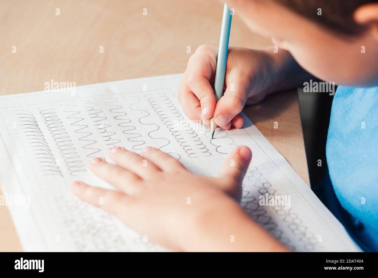 Nahaufnahme von Schuljunge tun Schreiben Aufgabe. Vorschreiben Übung, um die Hand für Schreiben Briefe vorzubereiten. Konzept der Kindererziehung Stockfoto