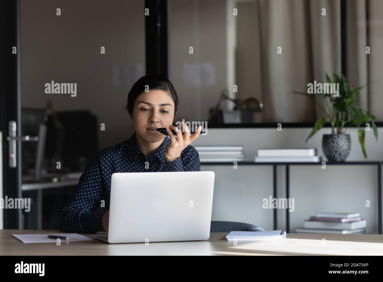Selbstbewusste indische Geschäftsfrau mit Laptop, Sprachnachricht auf dem Telefon aufzeichnen Stockfoto