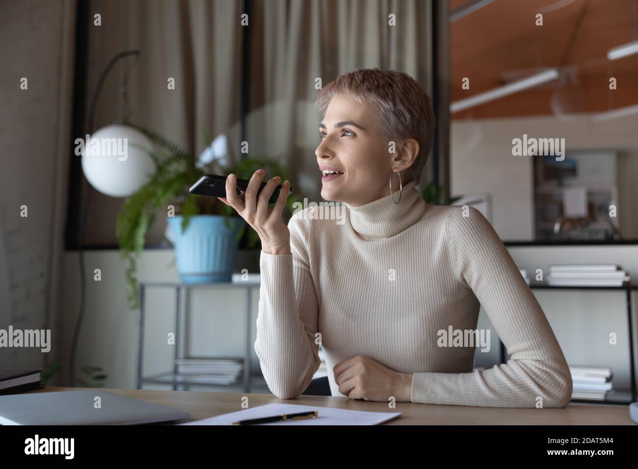 Lächelnde Geschäftsfrau, die im Büro Sprachnachrichten am Telefon aufzeichnet Stockfoto