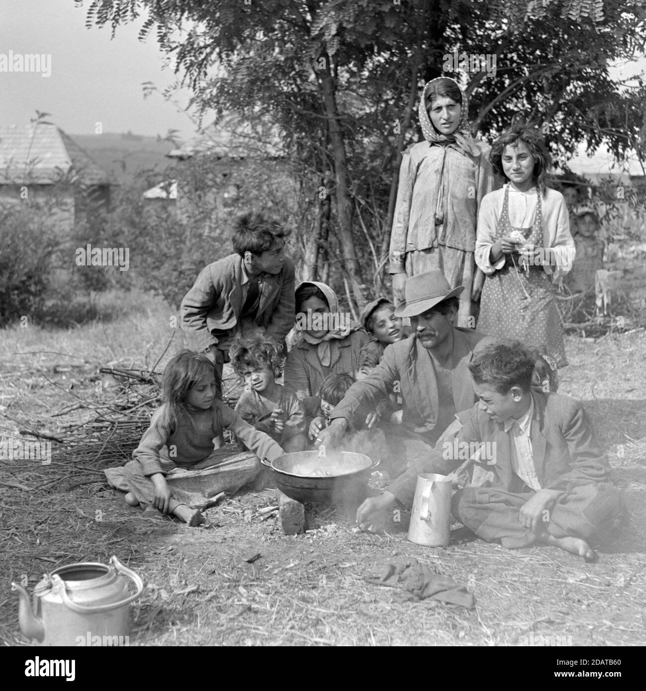Große roma Zigeunerfamilie versammelt in abgelegt am Stadtrand Von Dorf Kochen Mahlzeit mit Topf auf offenem Feuer 60er Jahre ungarn Stockfoto