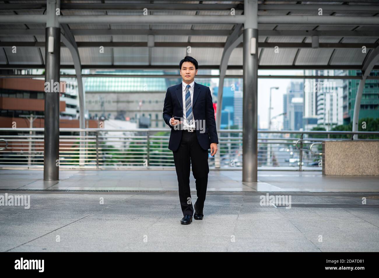 Geschäftsmann im Anzug zu Fuß und mit Smartphone in der Stadt Stockfoto