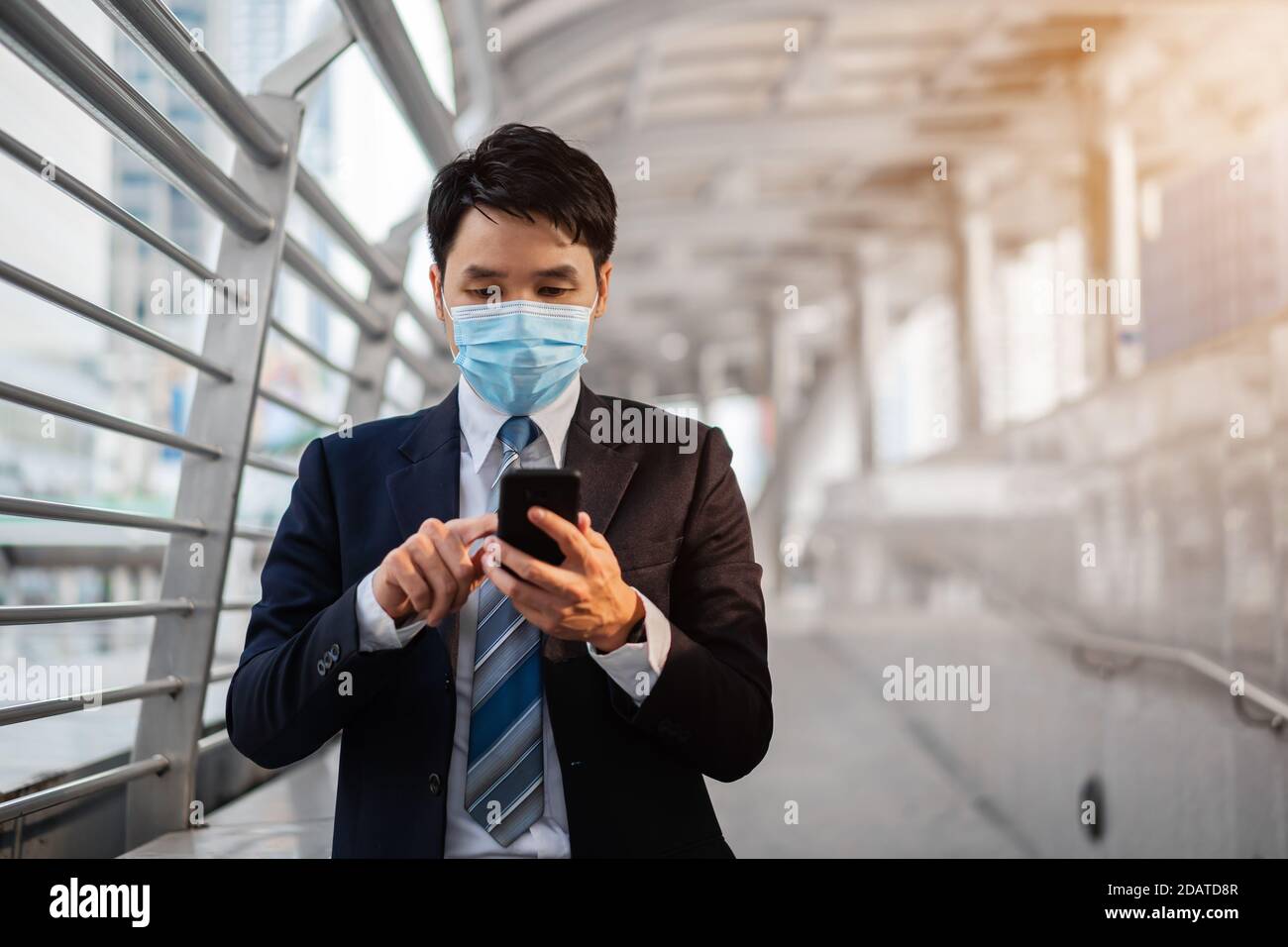 Business-Mann mit einem Smartphone und trägt medizinische Maske während Coronavirus (covid-19) Pandemie in der Stadt Stockfoto