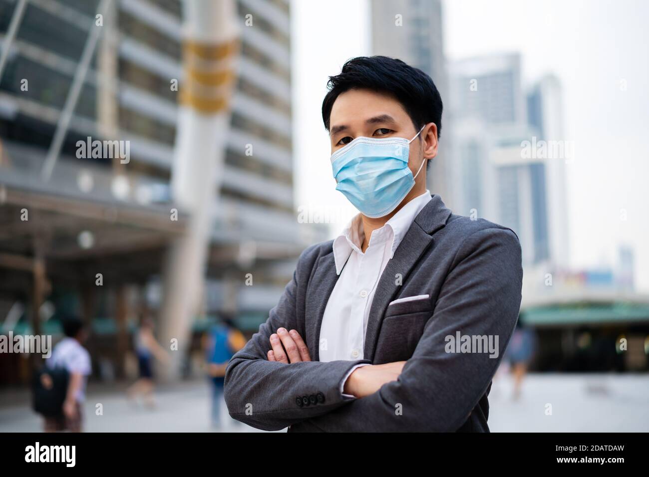 Business-Mann mit gekreuzten Armen und trägt medizinische Maske während Coronavirus (covid-19) Pandemie in der Stadt Stockfoto