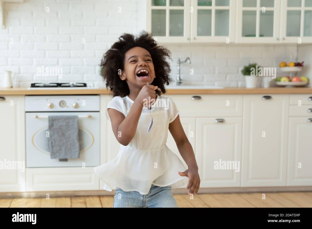 Überglücklich kleines afroamerikanisches Mädchen, das Gabel hält und singt Stockfoto