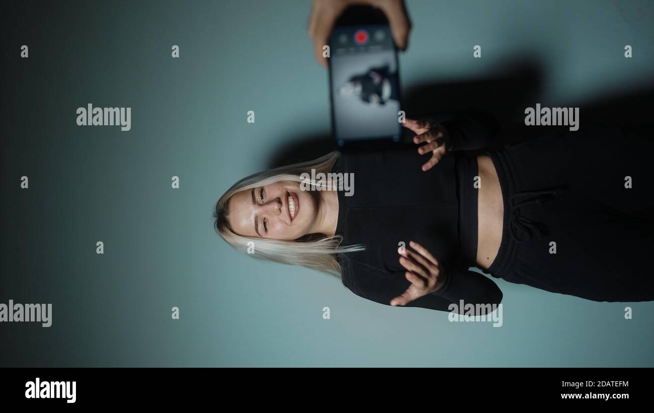 Junge blonde schöne attraktive Frau nimmt Video vlog Mit Telefon in Cyan-Farbe Studio-Hintergrund Stockfoto