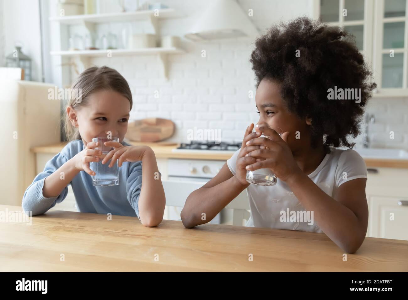 Afroamerikanische und kaukasische niedliche kleine Mädchen trinken reines Wasser Stockfoto