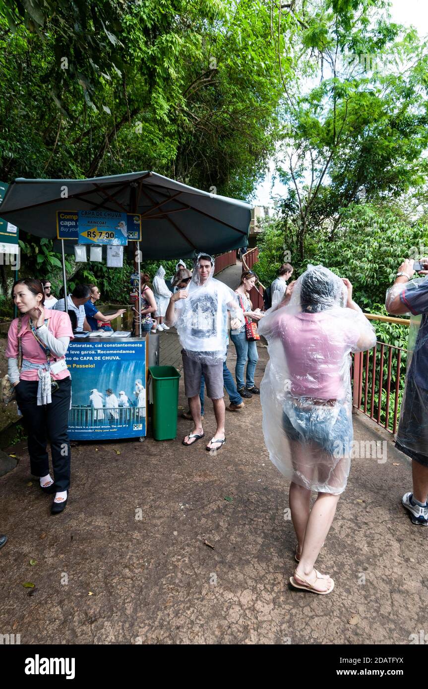 Besucher ziehen ihre gekauften Kunststoff-macs an einem nassen mac an Bewahren Sie sich vor dem Einweichen von den Wasserfällen Spray auf Die Iguazu Wasserfälle im Nati Stockfoto