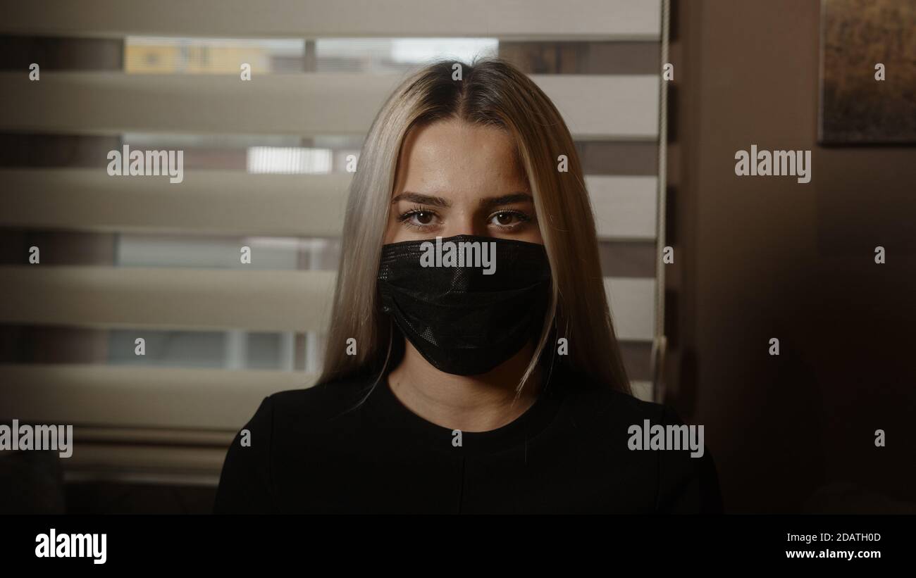 Charmante junge schöne blonde Frau bei der Arbeit, die ihre schwarze Maske, Pandemie und Büro Arbeitskonzept Stockfoto