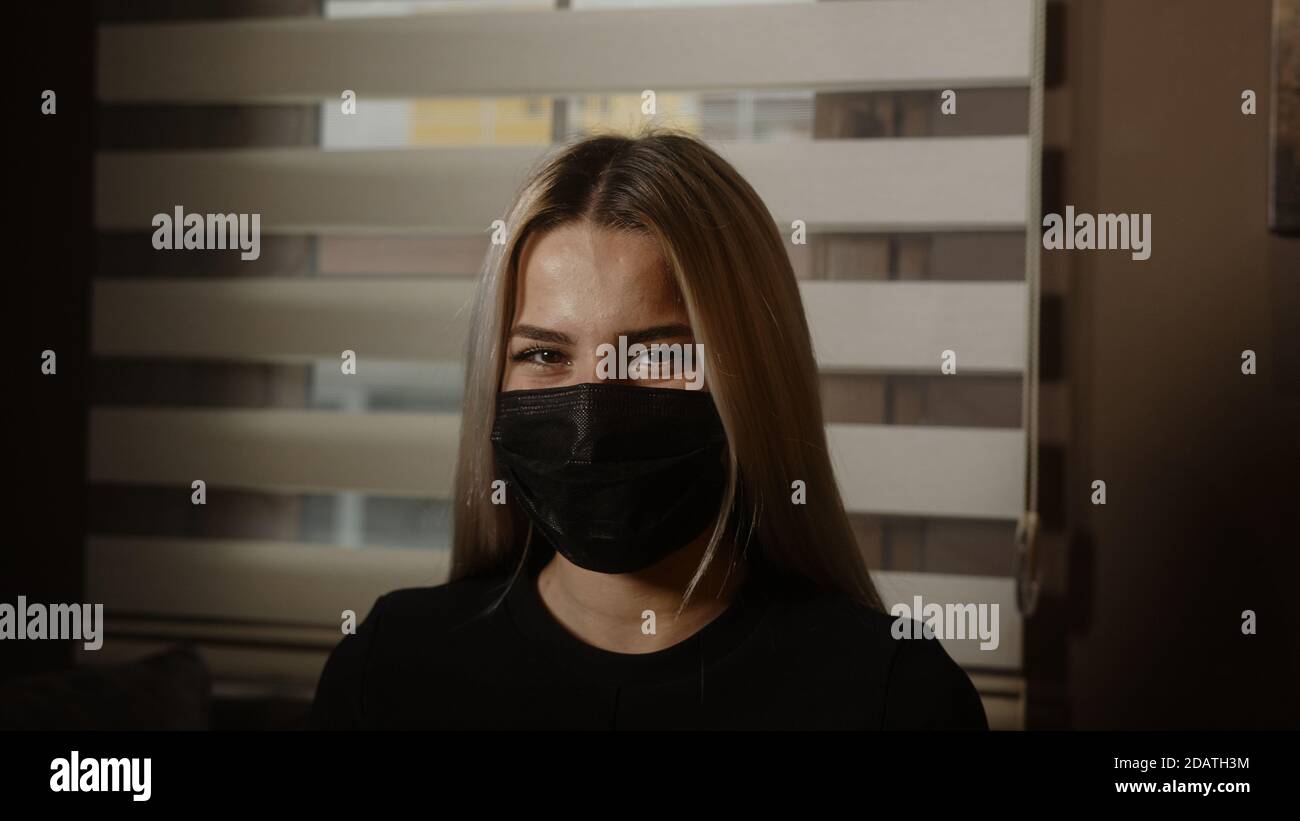 Charmante junge schöne blonde Frau bei der Arbeit, die ihre schwarze Maske, Pandemie und Büro Arbeitskonzept Stockfoto