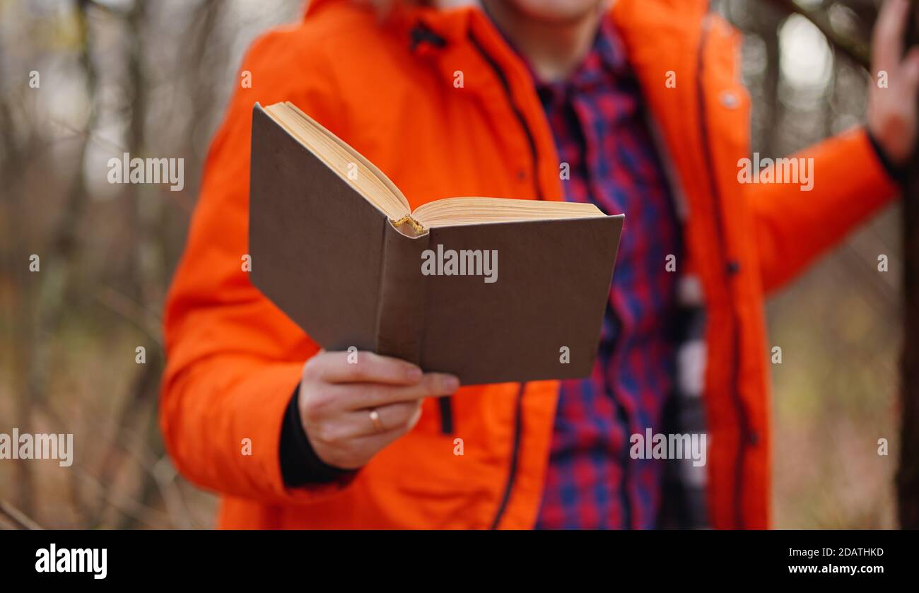 Nahaufnahme der Hand des Menschen mit Buch. Nicht erkennbarer Mann hält Buch, im Wald stehend Stockfoto