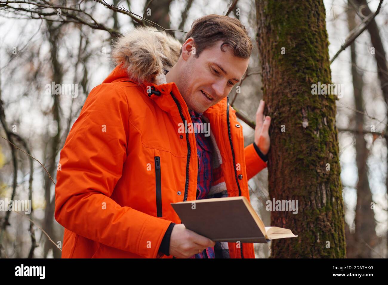 Erwachsene Mann in orange Jacke liest Buch im Herbst Wald. Junger Mann ruht mit Buch an der frischen Luft, genießt seine Freizeit Stockfoto