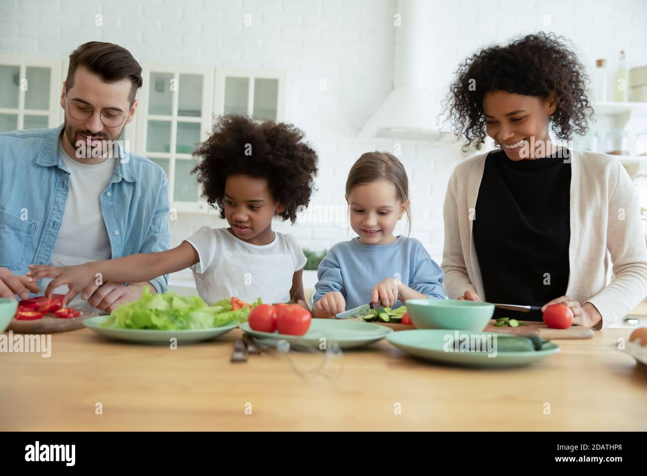Glückliche multirassische Familie mit Kindern, die Salat kochen, Gemüse zusammen schneiden Stockfoto
