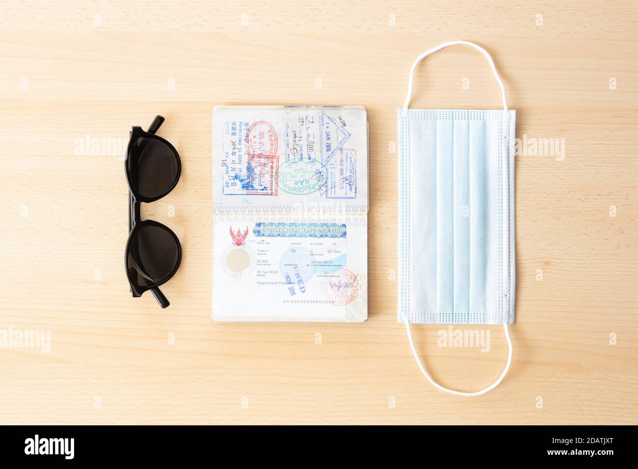 Sicheres Reisekonzept, Gesichtsmaske, Reisepass und Sonnenbrille sind auf einem Holztisch angeordnet. Stockfoto