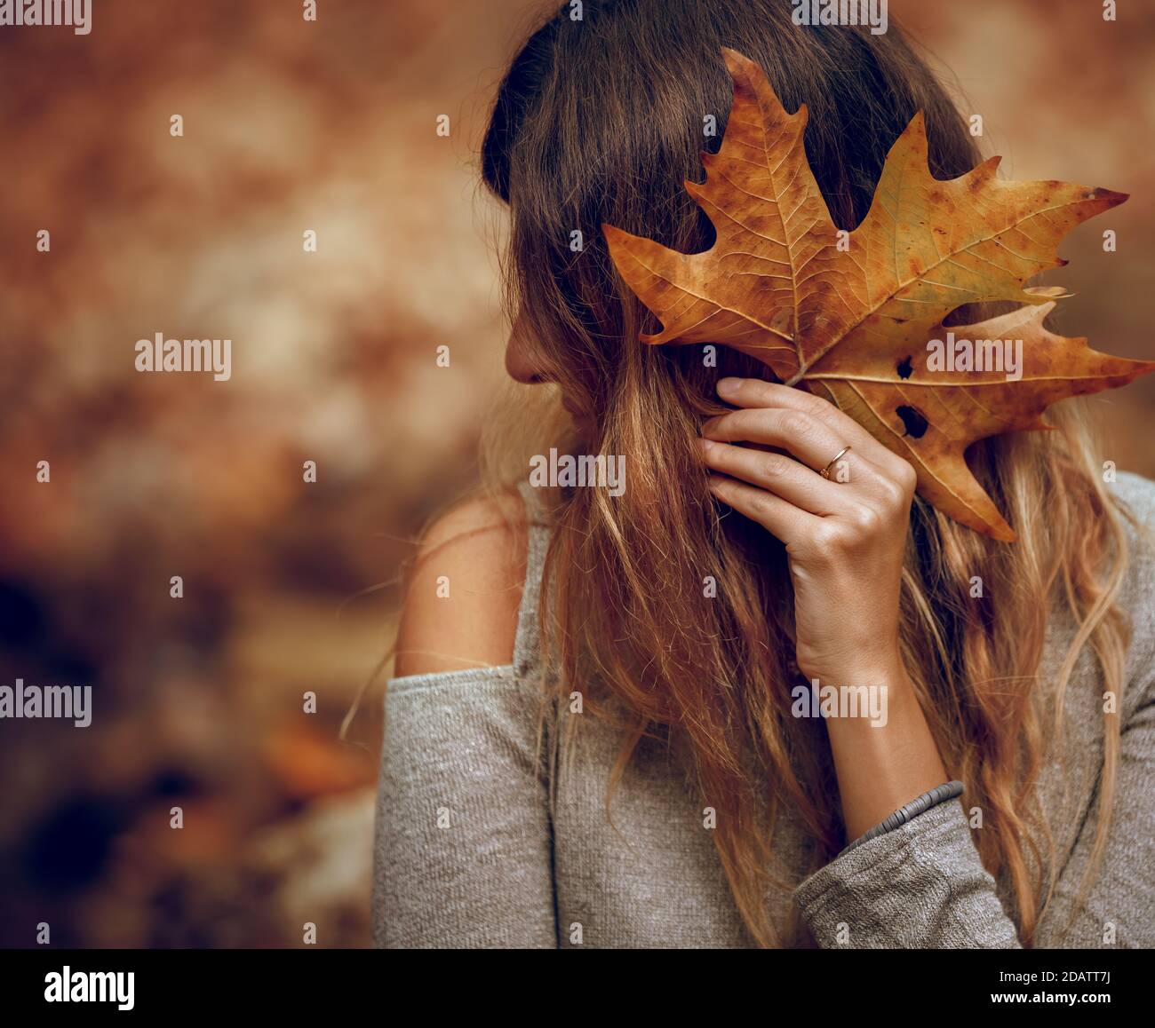 Schönes junges Model posiert im Herbstpark. Deckt die Vorderseite mit trockenem Ahornblatt ab. Schönheit der Natur im Herbst. Stockfoto