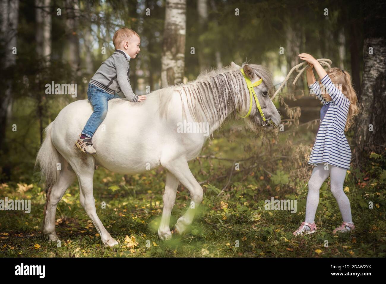 Kleine blonde Mädchen führenden Pony durch Zaum mit ihrer jüngeren Bruder Stockfoto