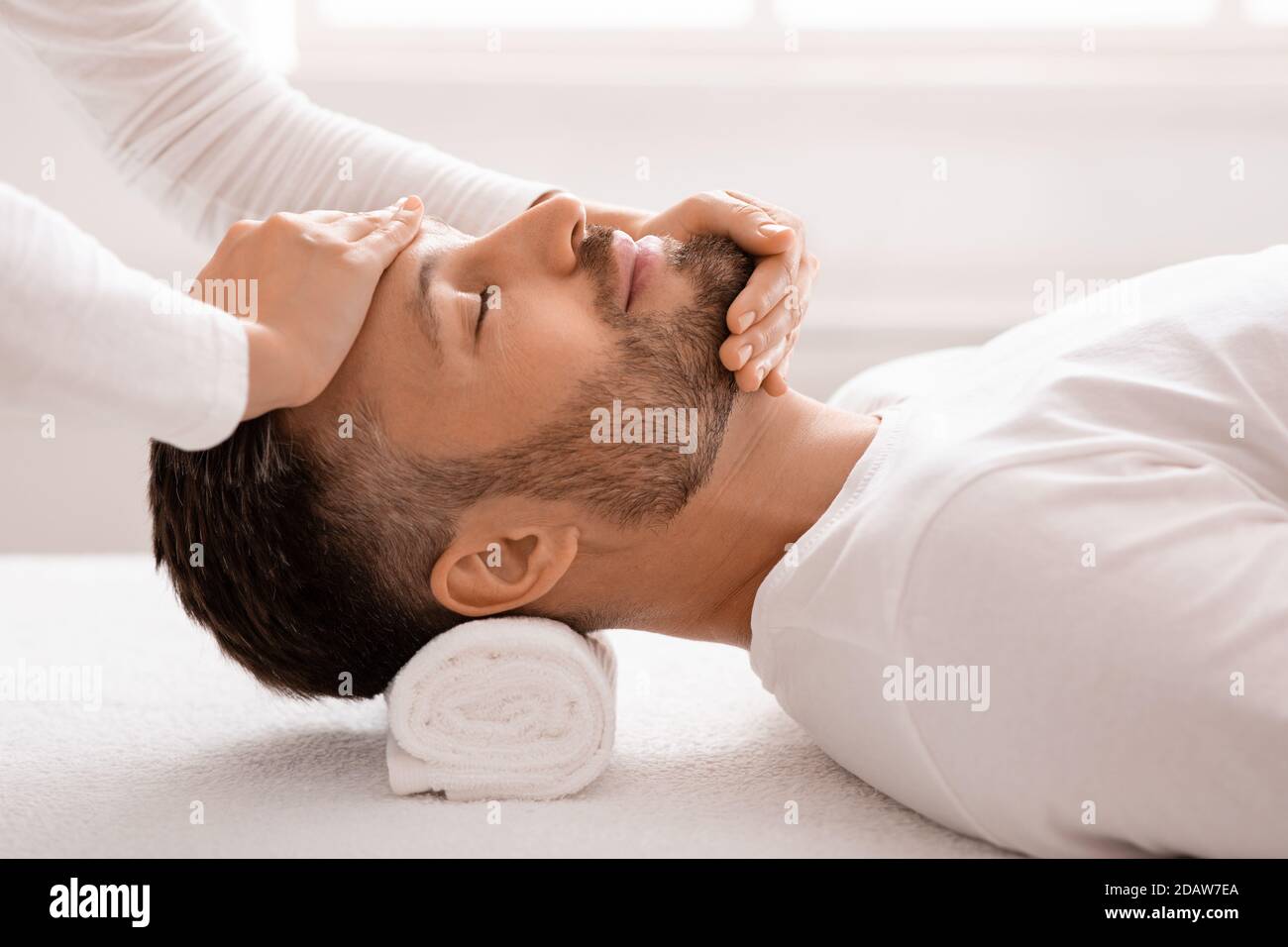 Schlafender Mann bekommt eine heilende Gesichtsmassage im Spa Stockfoto